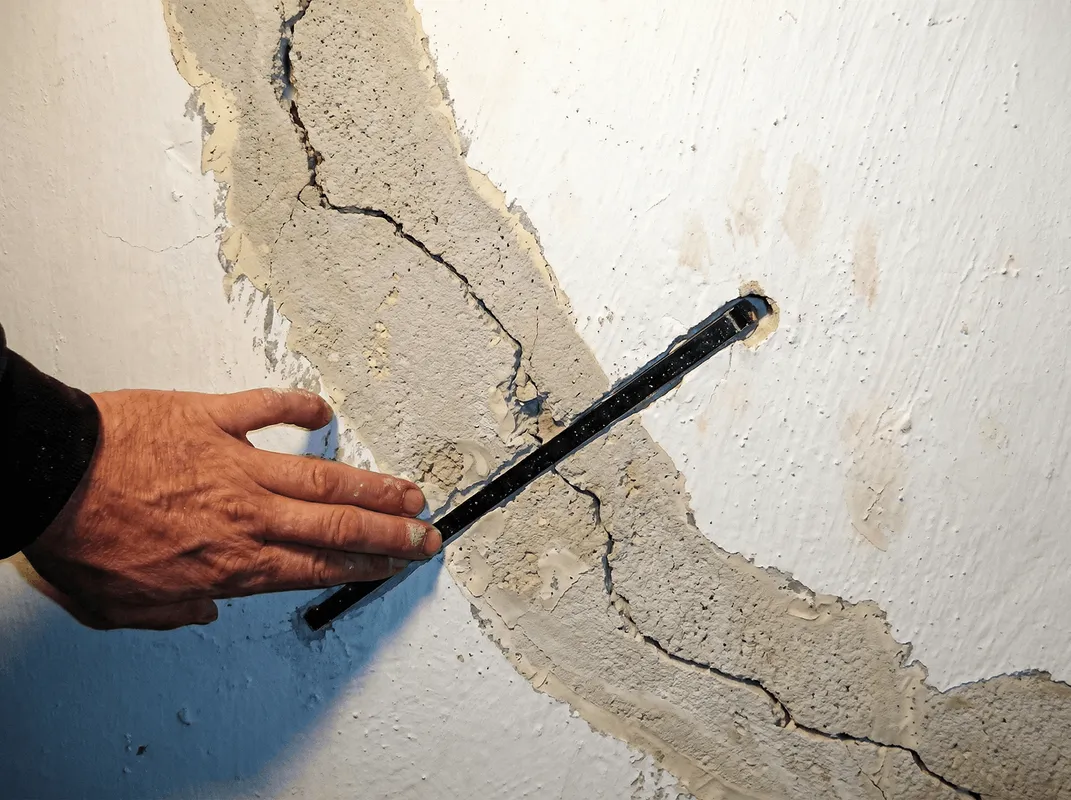 A wall with a large crack is being inspected by a professional in Syracuse, NY